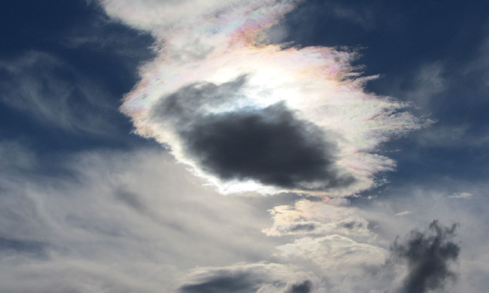 An iridescent cloud lit from behind by the sun, against a dark blue sky